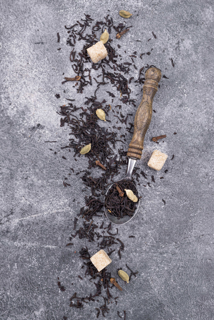 Ekliv Shilajit Gold Label appears as dark, coarse resin-like pieces scattered with pale chunks and a wooden-handled metal scoop.