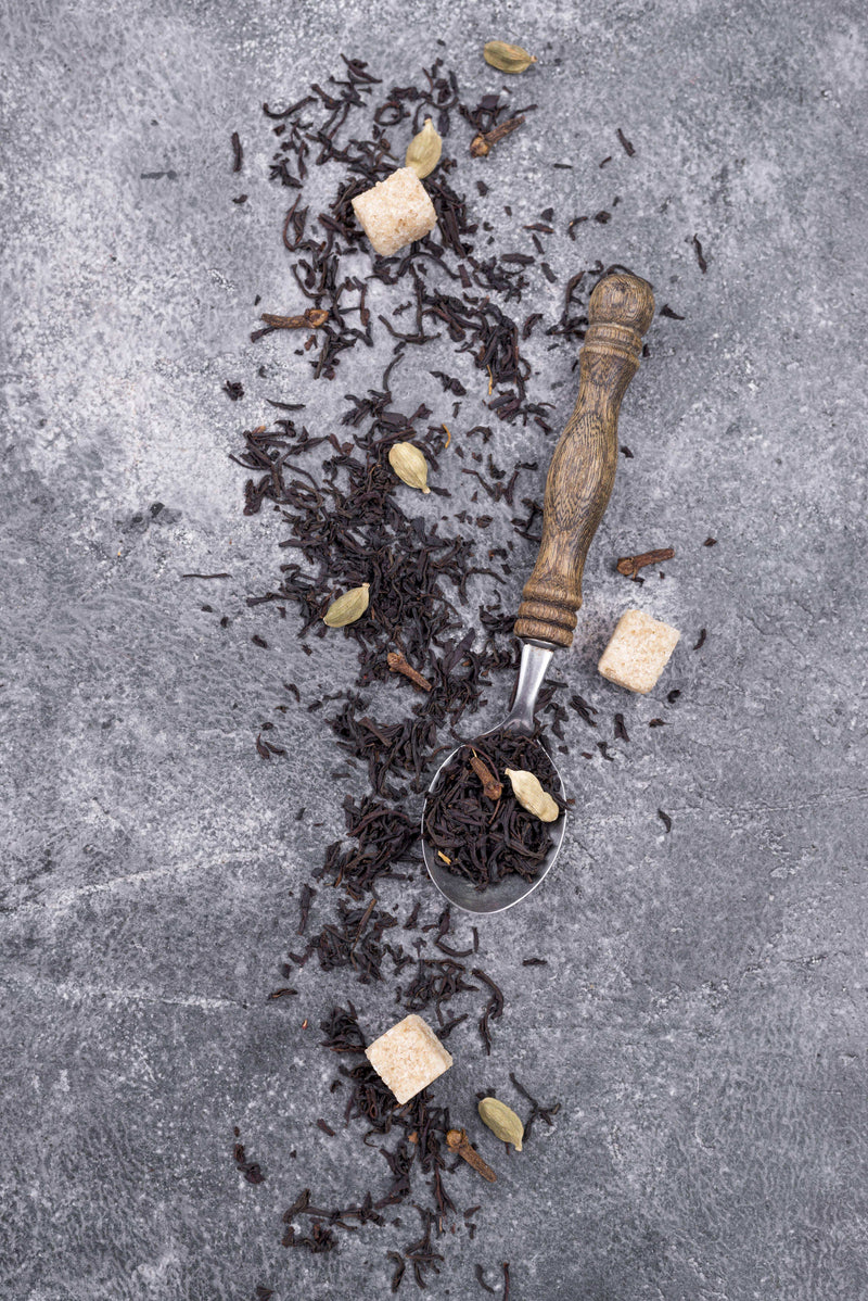 Ekliv Shilajit Gold Label appears as dark, coarse resin-like pieces scattered with pale chunks and a wooden-handled metal scoop.